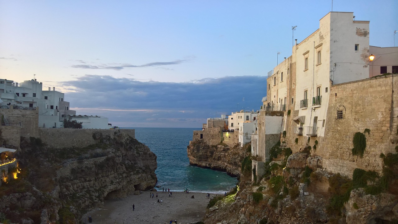 Vista panoramica di Polignano a Mare al tramonto, con il mare blu e le scogliere bianche.