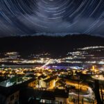 Vista notturna del borgo trentino con cielo stellato e monti sullo sfondo.