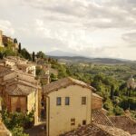 Vista panoramica su colline toscane e vigneti nel borgo nascosto, con un calice di vino in primo piano.