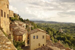 Vista panoramica su colline toscane e vigneti nel borgo nascosto, con un calice di vino in primo piano.
