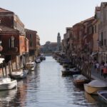 Turista sorpreso dai prezzi elevati in un hotel di Venezia, con cartelli di avviso sullo sfondo.