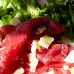 Bresaola affettata servita su un tagliere di legno con spezie e erbe aromatiche.