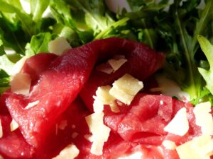 Bresaola affettata servita su un tagliere di legno con spezie e erbe aromatiche.