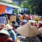 Un venditore ambulante in un mercato turistico affollato, con turisti che osservano le merci.