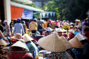 Un venditore ambulante in un mercato turistico affollato, con turisti che osservano le merci.