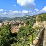 Panorama mozzafiato del borgo piemontese con colline verdi e cielo azzurro.