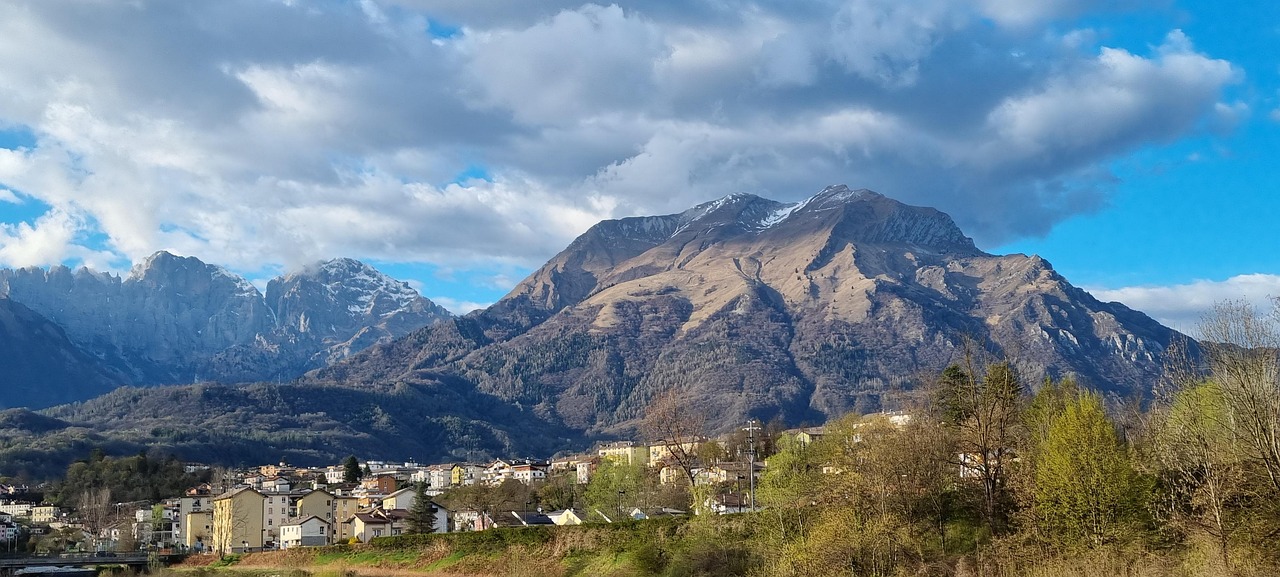 Panorama delle montagne lombarde con vette innevate e boschi verdi, ideale per escursioni e relax.